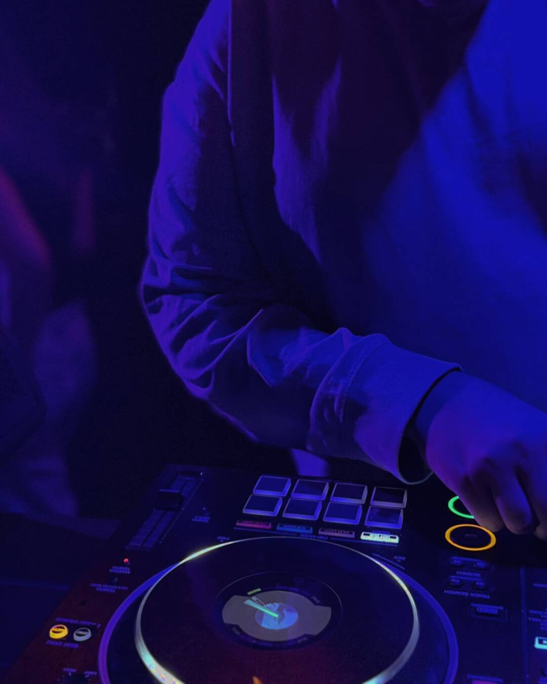 A DJ behind the decks under the Cassette neon sign